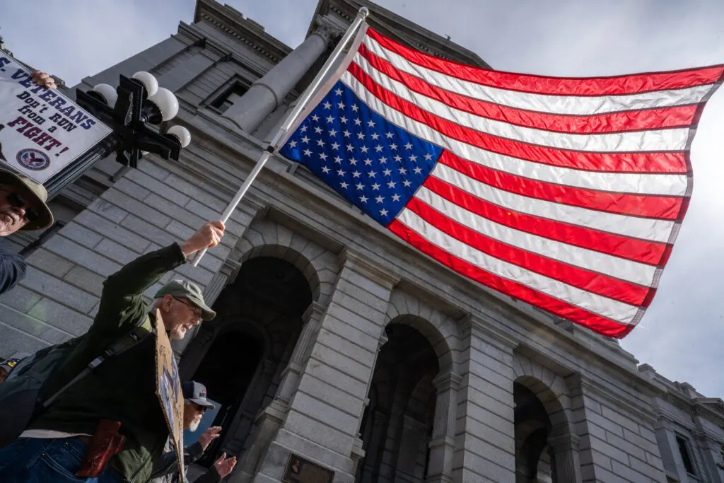 Veterans and supporters gather at the Denver State Capitol on March 14, holding American flags and signs demanding accountability.